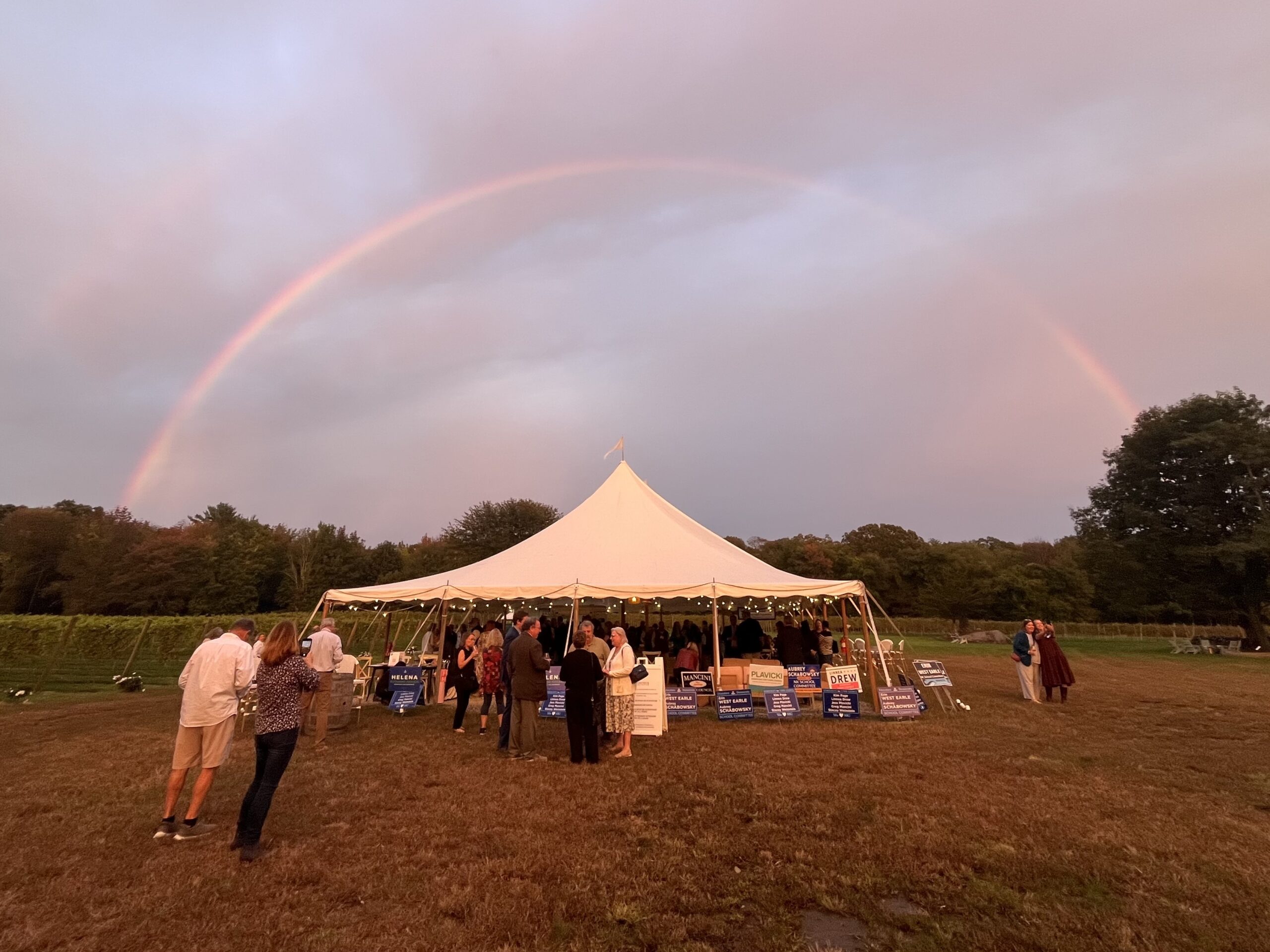 Rainbow over a tent with people talking and posing in front.